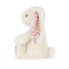 a white stuffed animal with pink flowers on it's ears, sitting in front of a white background