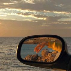 a person's hand is seen in the side view mirror of a car near the ocean