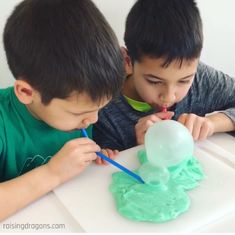 two young boys sitting at a table with green frosting on them and one boy is using a toothbrush to brush his teeth