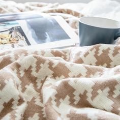 a coffee cup sitting on top of a bed next to a magazine