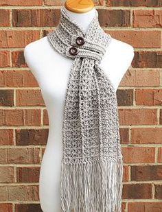 a white mannequin wearing a gray knitted scarf with buttons and fringes