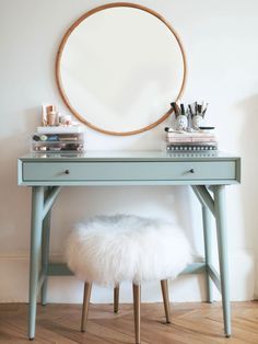 a blue desk with a round mirror above it and a white fur stool in front of it