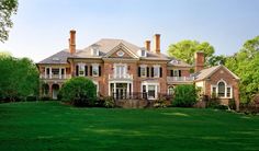 a large brick house with many windows and balconies on the top floor, surrounded by lush green grass