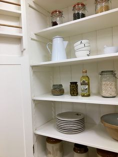 an open pantry with white shelves filled with dishes and jars on top of each shelf