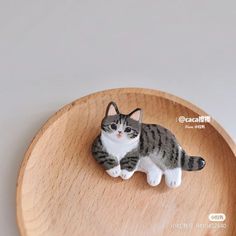 a small cat figurine sitting on top of a wooden plate with white and gray stripes