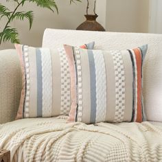 a white couch with two pillows and a blanket on it next to a potted plant