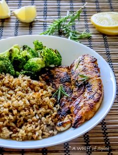 a white plate topped with meat and rice covered in broccoli next to lemon wedges