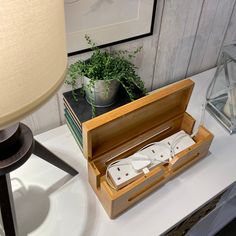 an open wooden box sitting on top of a table next to a lamp and potted plant