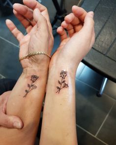 two people holding hands with tattoos on their arms and one has a flower tattoo on the wrist