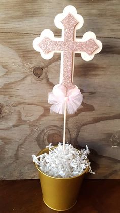 a pink cross on top of a cup filled with shredded white paper next to a wooden wall