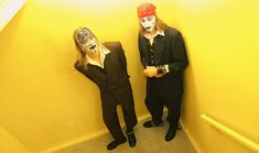 two people with painted faces standing next to each other in a stairwell area, one wearing a red bandana and the other wears a black suit