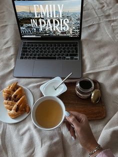 a laptop computer sitting on top of a bed next to a cup of tea and doughnuts