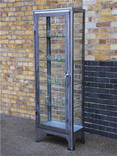 a tall metal and glass display case in front of a brick wall