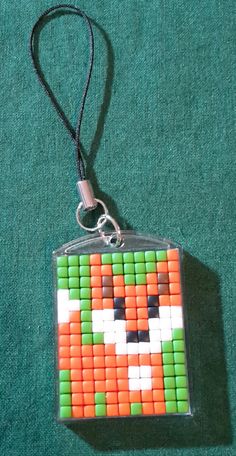 an orange and green bead keychain hanging from a black cord on a green surface