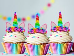 three cupcakes with white frosting and unicorn ears on them, surrounded by confetti