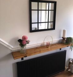 a vase with flowers on top of a wooden shelf next to a radiator