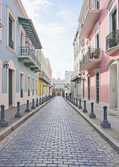 a cobblestone street lined with pastel colored buildings and balconies on either side