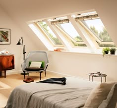 a bed sitting under three windows in a bedroom next to a desk and chair with a laptop on it