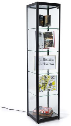 a glass display case filled with books and magazines on top of a white floor next to a wall