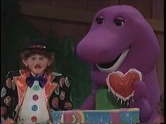 a woman standing next to a purple dinosaur with a heart on it's chest