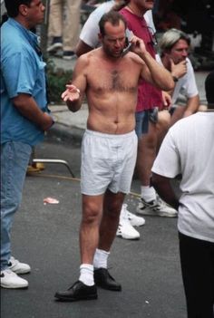 a shirtless man talks on his cell phone while standing in the middle of a street