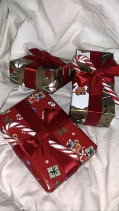 three wrapped presents sitting on top of a white bed covered in red and gold wrapping paper