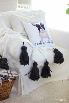 a white couch with black tassels on it and a pillow that says i wake up late