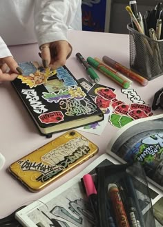 a person is doing some art work on an open book with markers and pencils