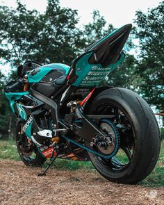 a motorcycle parked on the side of a dirt road next to some grass and trees