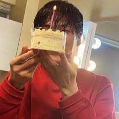 a man holding up a frosted cupcake with a lit candle on it in front of his face