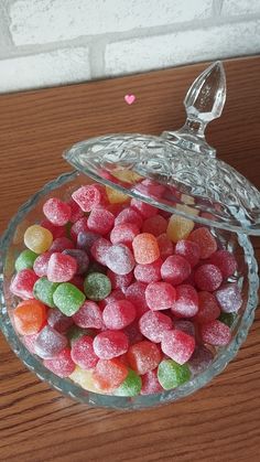 a glass bowl filled with candy hearts on top of a wooden table