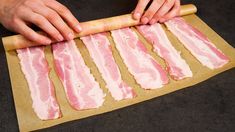 a person rolling up bacon on top of a wooden board