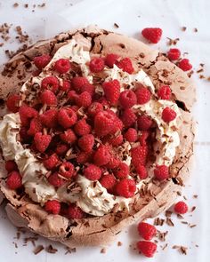 a chocolate cake with whipped cream and raspberries on top, sitting on a white surface