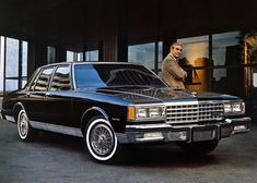 a man standing next to a black car in front of a building