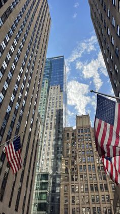 two american flags are flying in front of tall buildings