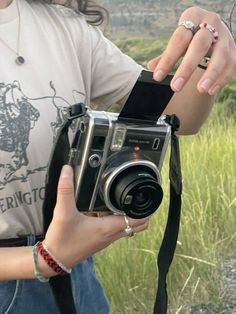 a woman holding a camera in her right hand while standing next to a grassy field