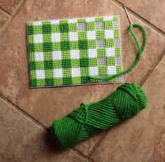 a green and white checkered table cloth next to a spool of thread on the floor