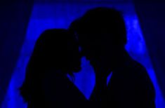 the silhouette of a man and woman kissing in front of a blue curtain with curtains behind them