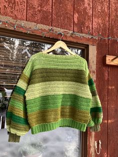 a green and yellow sweater hanging on a clothes line in front of a red barn