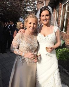 two women standing next to each other in front of a building wearing wedding gowns