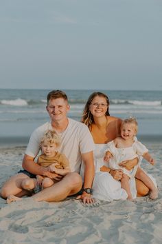 a family is sitting on the beach with their two children and an adult in front of them