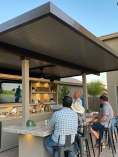 several people sitting at a bar watching tv in the back yard with their backs to the camera