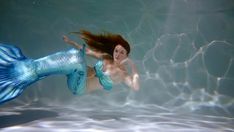 a mermaid is swimming in the water with her hair blowing back and looking at the camera