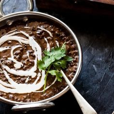 a bowl filled with beans and sour cream on top of a wooden table next to spoons