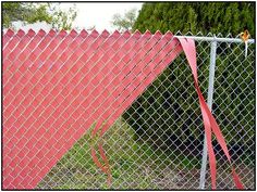 a fire hydrant sitting next to a chain link fence with a red ribbon on it