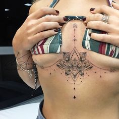 a woman's stomach with tattoos on it and her hands holding the top part of her belly