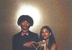 a man and woman standing next to each other in front of a wall holding a cake