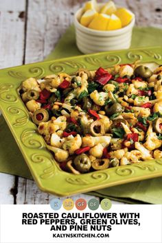 roasted cauliflower with red pepper and pine nuts on a green platter next to a bowl of lemons