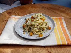 a white plate topped with pasta on top of a wooden table next to a cup