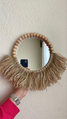 a person is holding a mirror with some wood beads on it and a tassel hanging from the wall